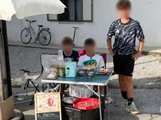 I tre amici dietro al loro banchetto con limonata, caffè e dolcetti