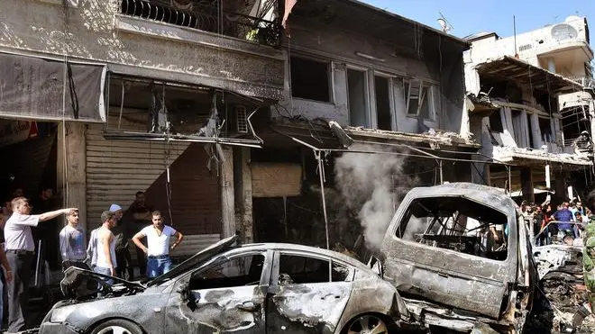 A handout photo made available by Syrian Arab News Agency (SANA) shows citizens inspecting damaged buildings and burnt-out cars at the site of a car bomb explosion in Jaramana residence area in rural Damascus, Syria, 25 July 2013. According to SANA, the explosion caused casualties among citizens. ANSA/SANA HANDOUT HANDOUT EDITORIAL USE ONLY/NO SALES