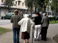 Due badanti accompagnano due anziani in un giardino