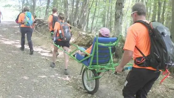 I volontari dei Cai di Feltre mentre trasportano un disabile sul Monte Avena grazie a una joëlette