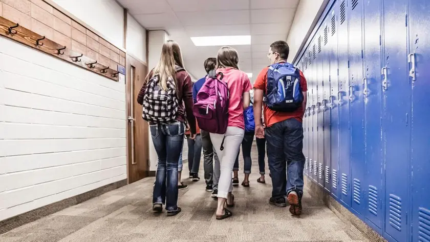 Rear view of high school students walking along school locker corridor