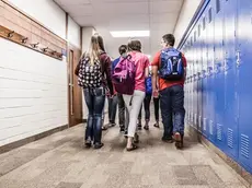 Rear view of high school students walking along school locker corridor